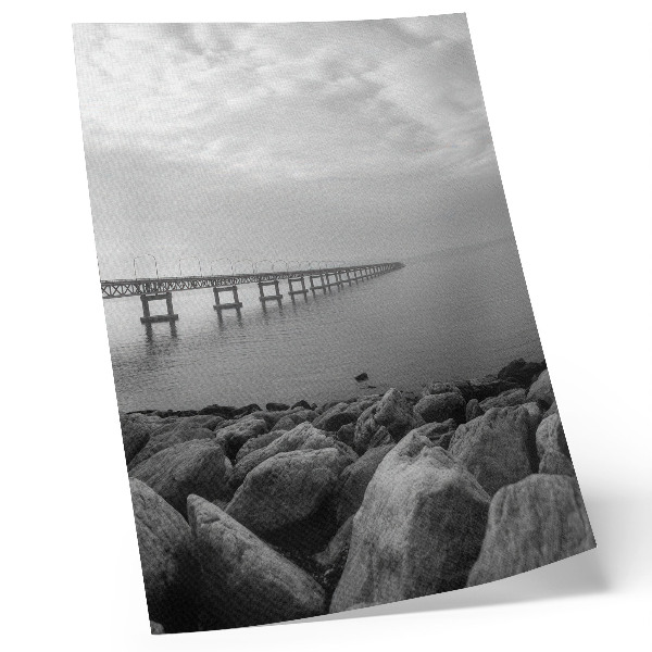 Wandposter Vreedzaam landschap, brug, rotsachtig strand, grijze lucht