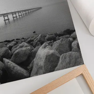 Wandposter vreedzaam landschap met een brug en een rotsachtig strand onder een grijze lucht
