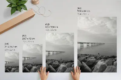 Wandposter vreedzaam landschap met een brug en een rotsachtig strand onder een grijze lucht