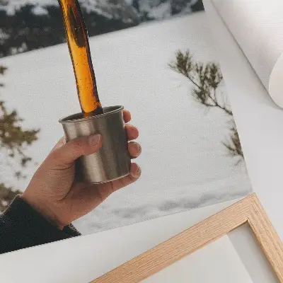 Decoratieve poster met afbeelding van een mok met een amberkleurige substantie, bergen en sneeuw