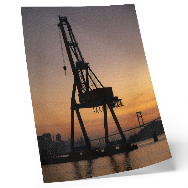 Wandposter Silhouet van een industriële kraan bij zonsondergang op een brug