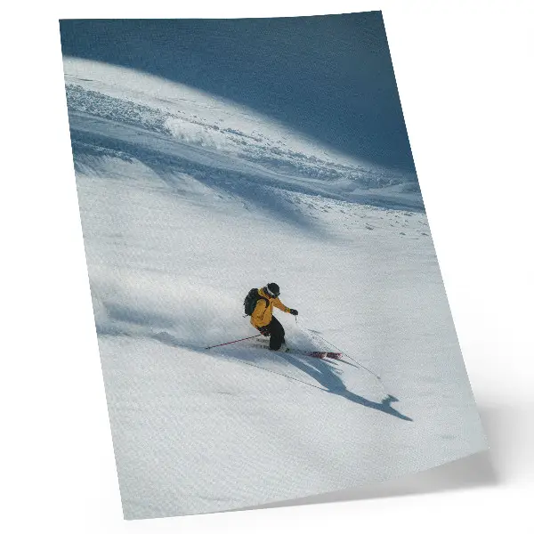 Poster skiër met een gele jas op een besneeuwde helling met schaduw
