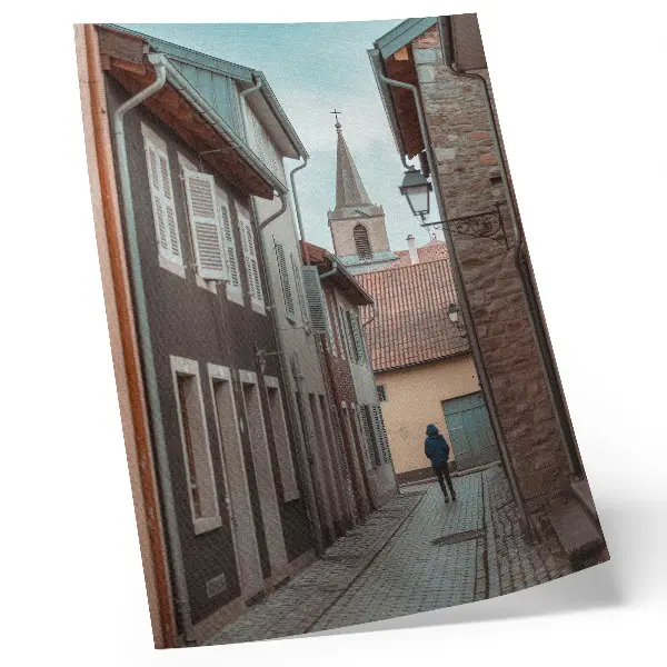 Wandposter smalle straat met huurkazernes, een toren en een persoon in een blauwe jas