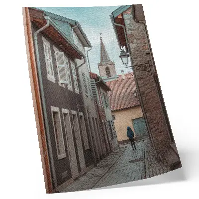 Wandposter smalle straat met huurkazernes, een toren en een persoon in een blauwe jas