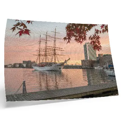 Poster zeilschip bij zonsondergang met een vredig stadsgezicht