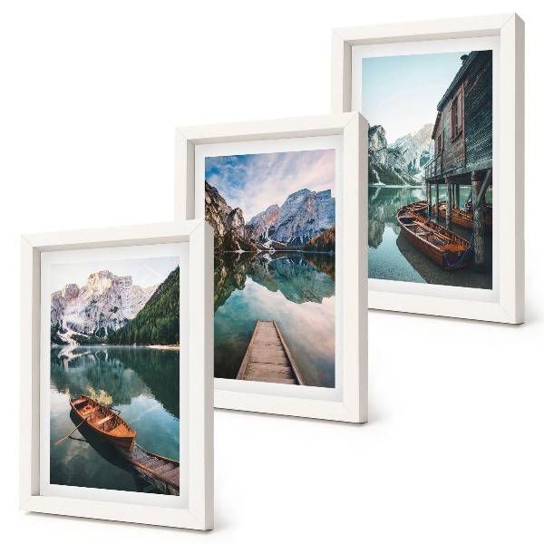 Set van ingelijste schilderijen Een meer in de bergen met bootjes en een houten hut.