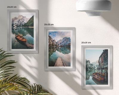Set van ingelijste schilderijen Een meer in de bergen met bootjes en een houten hut.