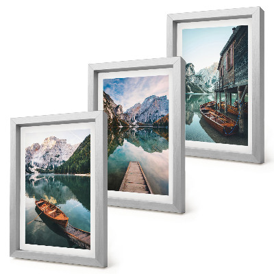 Set van ingelijste schilderijen Een meer in de bergen met bootjes en een houten hut.